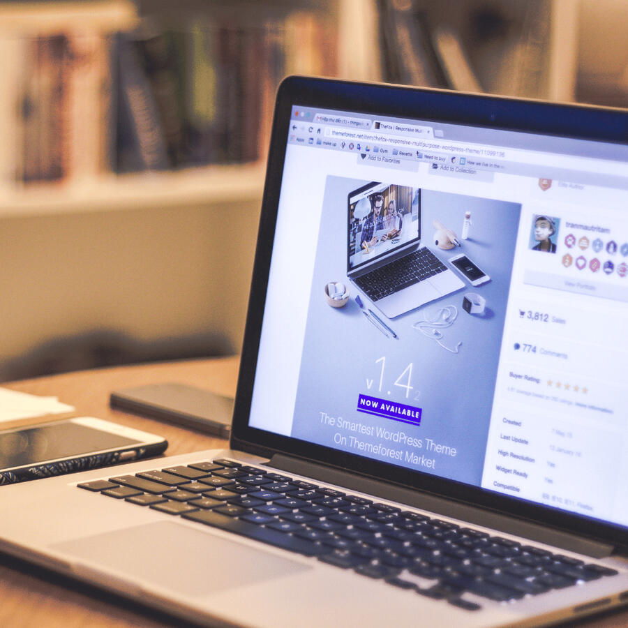 Image of a laptop and mobile device on a desk with a bookshelf in the background.